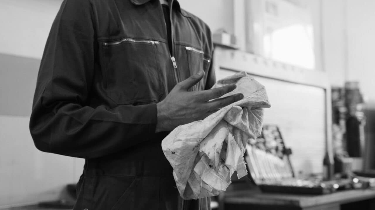 pexels-photo-8985705-8985705 Mechanic cleaning hands with cloth in a monochrome automotive workshop setting.